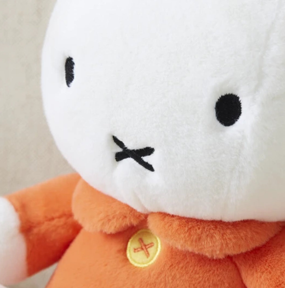 close up of Miffy Hug Me fluffy sitting plush toy wearing an orange outfit with a white collar and button detail.